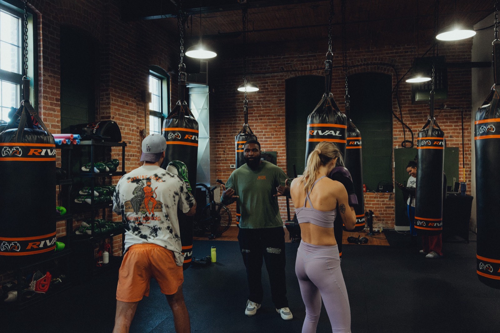 Members working the heavy bags in the South West Boxing Club gym, brick walls and tall windows behind them